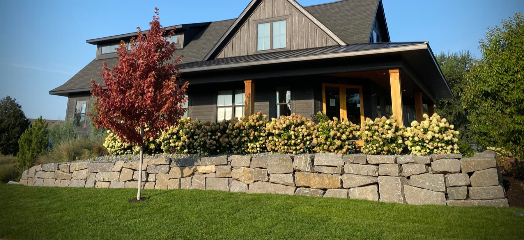 Finished natural-stone retaining wall with lawn and hydrangeas