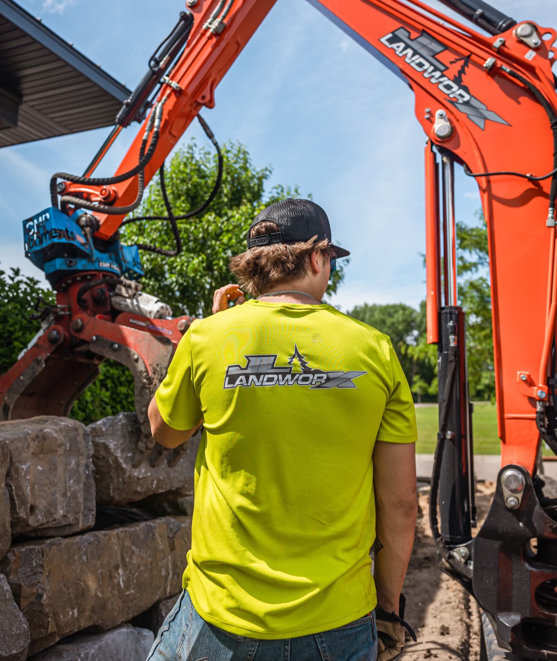 JL Landworx crew member beside an excavator placing boulders