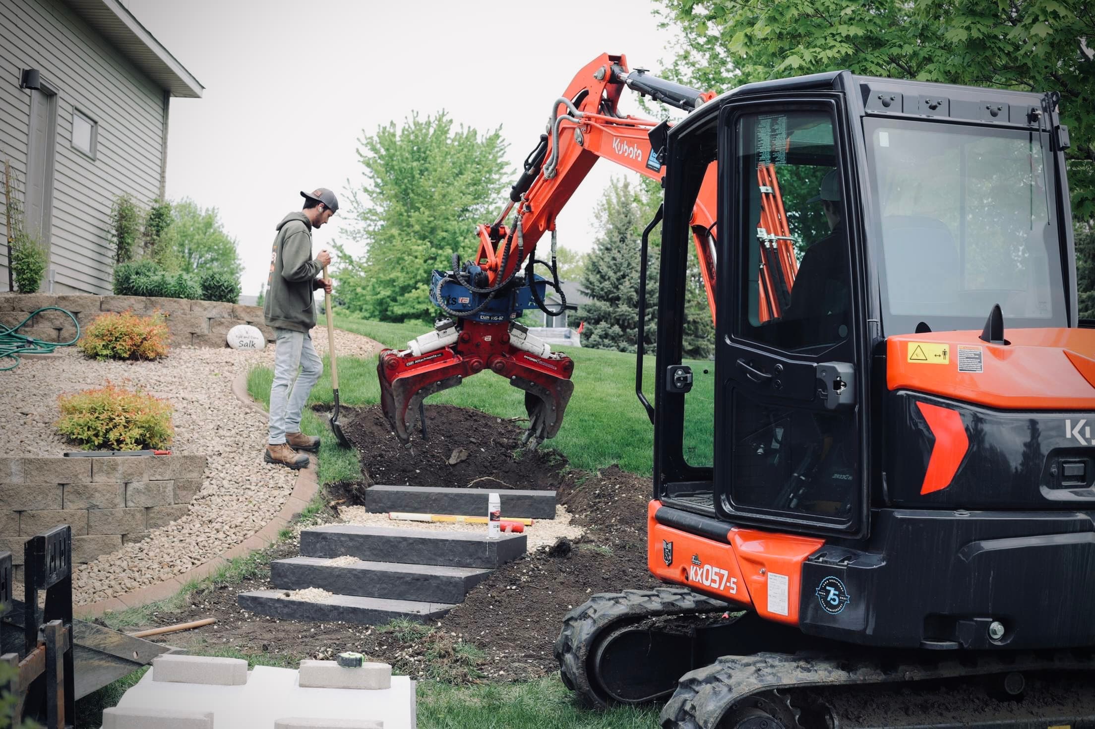 Crew member and compact excavator installing landscape steps