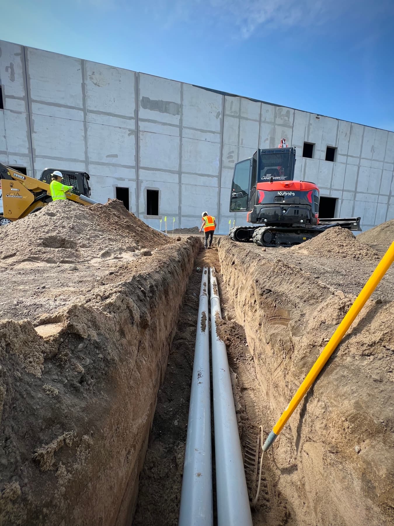 Excavator beside a deep utility trench at a commercial building